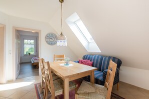 Et hyggeligt rum med et træspisebord, stole, en stribet sofa og et ovenlys.