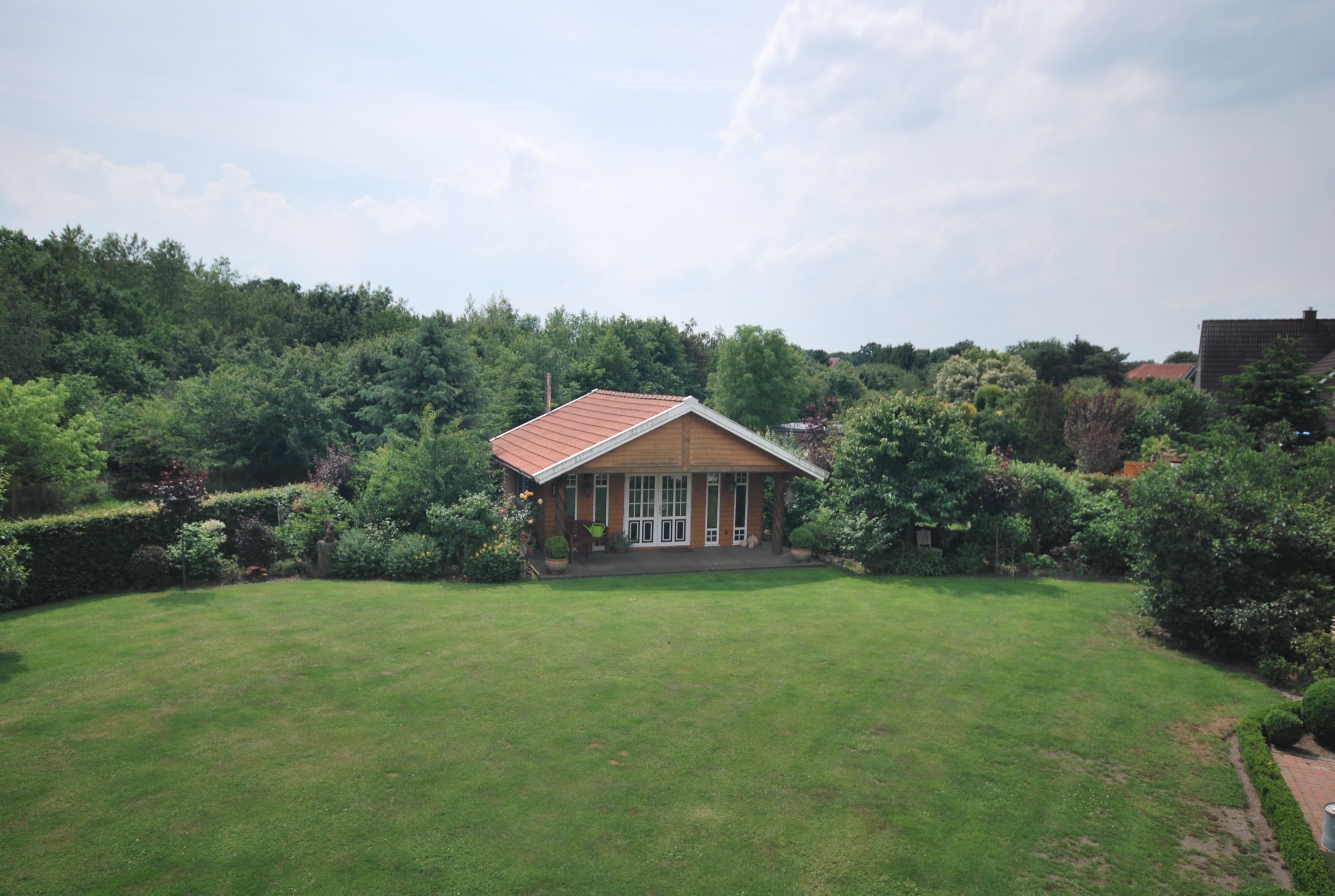 A house with a red roof, surrounded by a well-maintained lawn and dense greenery.