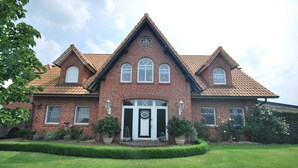 A large brick house with a symmetrical facade, a central entrance with a white door, and a triangular roof.