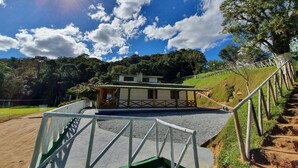 A traditional house with a wooden porch, surrounded by a gravel pathway and a metal railing. - Sítio Pedacinho do Céu na Serra de SC (Aguas Mornas)