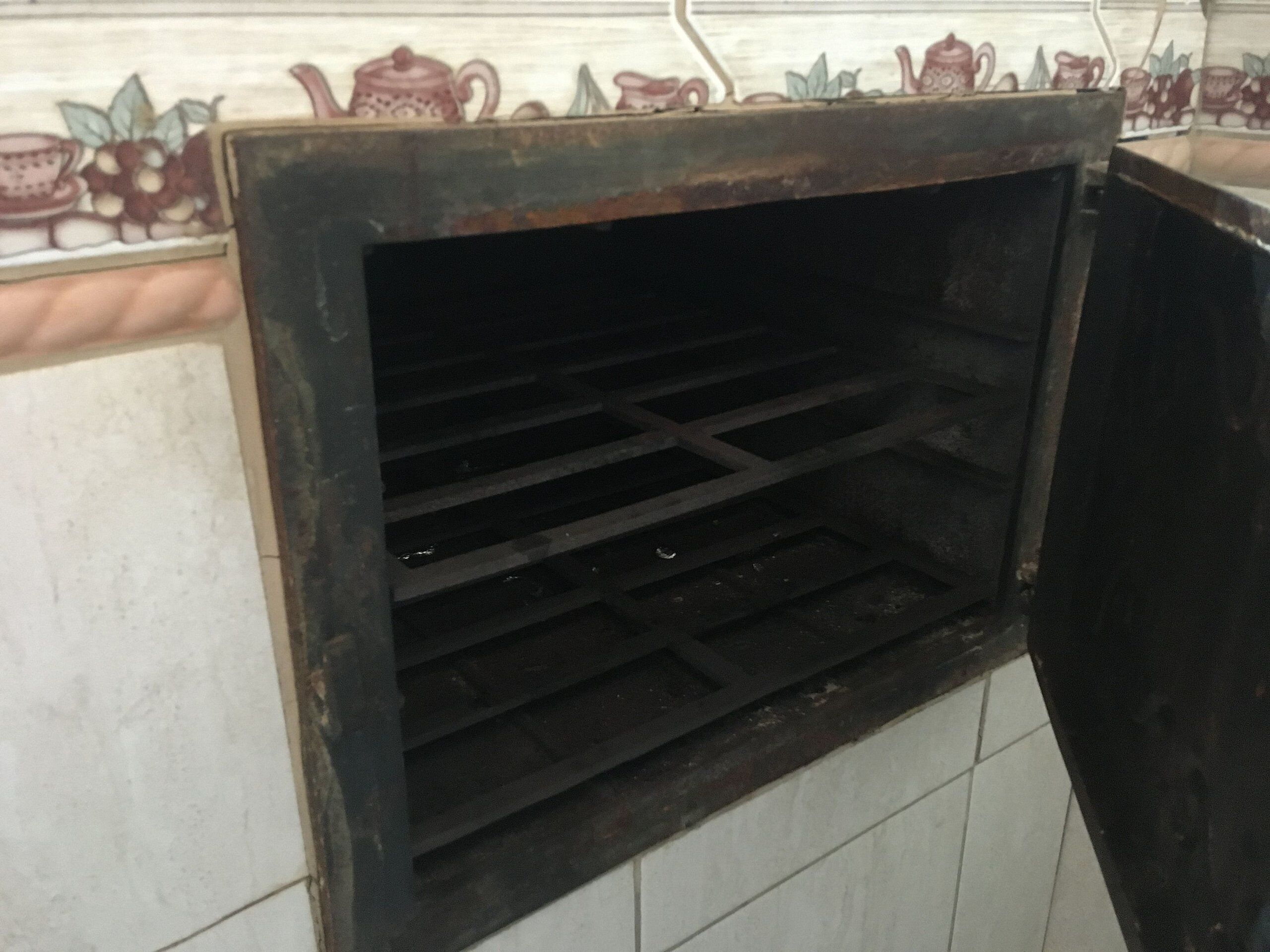 A kitchen with a tiled backsplash and a black oven with a metal rack inside.