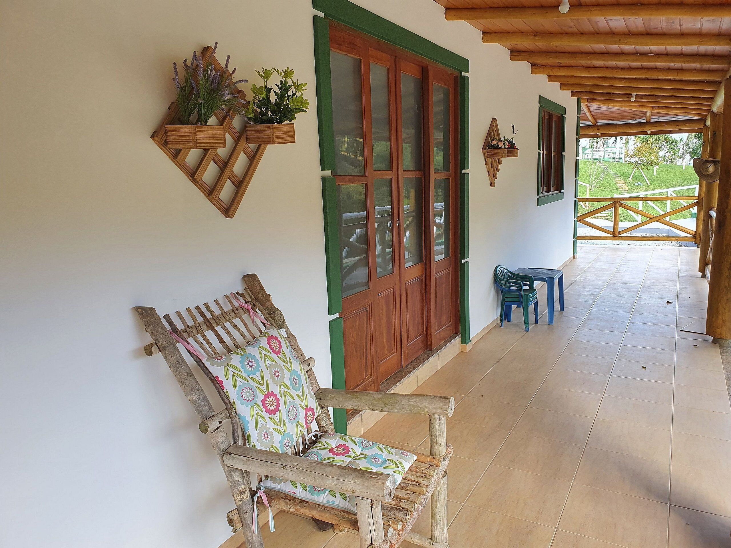 A wooden porch with a bench and a table, a wooden door, and a view of a garden.