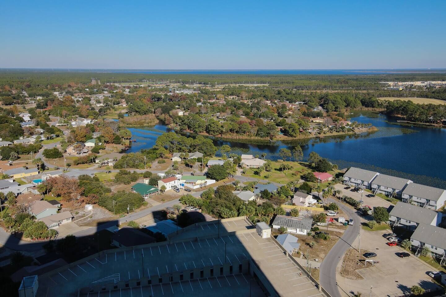An aerial view of a residential area with houses, a large parking lot, and a body of water.