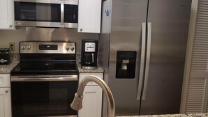 Eine Küche mit weißen Schränken, einem Edelstahl-Kühlschrank, einer Mikrowelle, einem Backofen, einer Kaffeemaschine und einem Spülbecken.