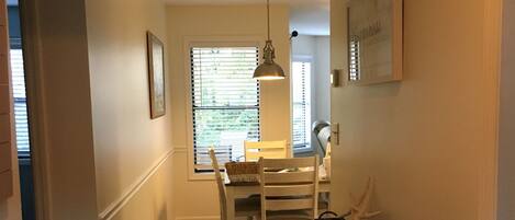 A narrow hallway with wooden flooring, a dining table with chairs, a hanging pendant light, and a small table with antlers and a basket.