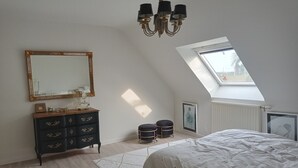 Un dormitorio con cama, tocador, espejo, candelabro, tragaluz y radiador.