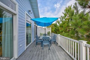 A deck with a table and chairs, a blue umbrella, and a white railing.