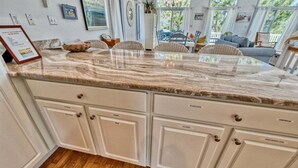 A kitchen with a marble countertop, white cabinetry, and a dining area with chairs and a table. - Bethany Beach * 4BR Luxury House (Bethany Beach)
