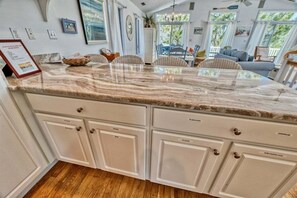 A kitchen with a marble countertop, white cabinetry, and a dining area with chairs and a table.