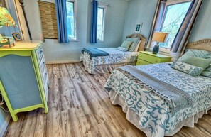 A bedroom with two beds, a desk, and a window with curtains.