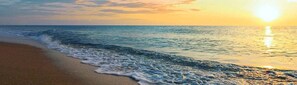 A beach with waves, a sunset, and a clear sky.