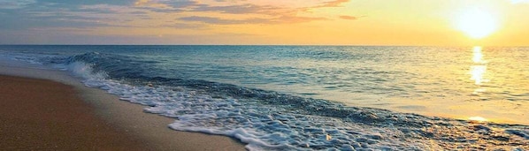 A beach with waves, a sunset, and a clear sky.