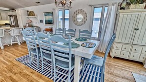 A dining area with a white table and blue chairs, a chandelier, a mirror, and a view of the ocean. - Bethany Beach * 4BR Luxury House (Bethany Beach)