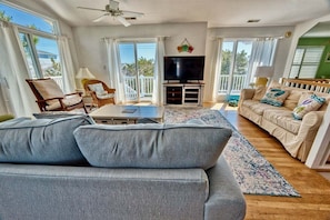 A living room with a sofa, chairs, a TV, and a balcony. - Bethany Beach * 4BR Luxury House (Bethany Beach)
