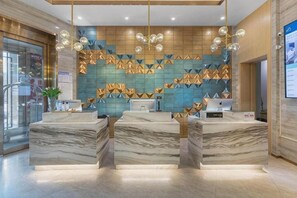Zona de recepción de hotel con mostradores de mármol, pared con diseño geométrico e iluminación colgante.
