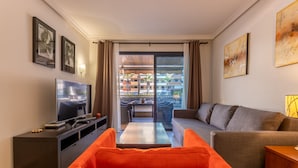 A modern living room with a television, orange sofa, grey sofa, and a dining area with a table and chairs. - Balcon de Los Gigantes 2A016 poolview (Acantilados de Los Gigantes)