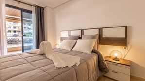 A bedroom with a large bed, a nightstand with a lamp, and a view of buildings through a sliding door. - Balcon de Los Gigantes 2A016 poolview (Acantilados de Los Gigantes)