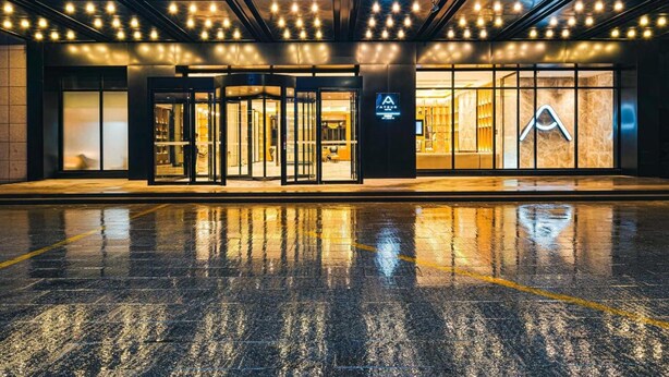 Entrada de hotel con diseño moderno, que presenta un letrero de neón y un frente de cristal.