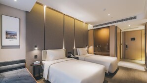 Habitación de hotel con dos camas, una mesita de noche, un cuadro enmarcado en la pared y una puerta que da a otra habitación.