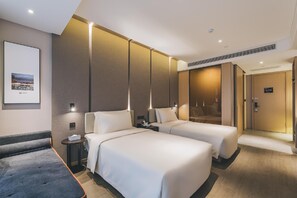 Habitació d'hotel amb dos llits, una tauleta de nit, un quadre al mur i una porta que dona a una altra habitació.