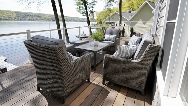 Terraza con mobiliario de mimbre, una mesa y vistas a un lago y casas.