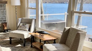 Una habitación acogedora con dos sillones, una pequeña mesa de madera y vistas a un lago a través de amplias ventanas.