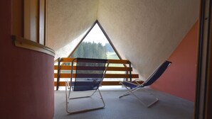 A room with a sloped ceiling, two reclining chairs, a wooden bench, and a view of trees through a triangular window.
