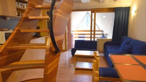 A compact living space with a spiral staircase, a sofa, a dining table, and a kitchen area.