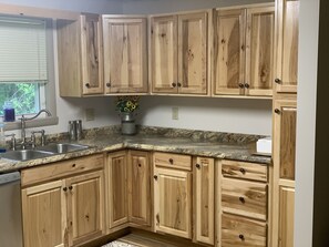 A kitchen with wooden cabinets, a granite countertop, a sink, and a window with blinds.