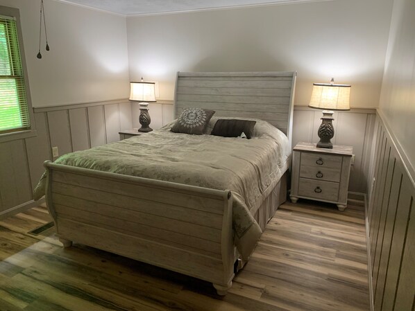 A bedroom with a wooden bed, two bedside tables with lamps, and a window with blinds.