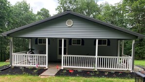 A single-story house with a porch, a small garden, and a lawn. - Cottage in the Woods (Warfordsburg)