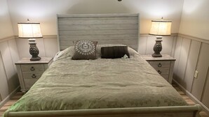 A bedroom with a wooden headboard, two bedside tables with lamps, a bed with patterned bedding, and a nightstand with a decorative lamp. - Cottage in the Woods (Warfordsburg)