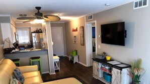 A living room with a beige sofa, a television mounted on the wall, and a kitchen area in the background. - 2BD/2BATH Villa! Near Beach! HHR Building 1! (Hilton Head Island)