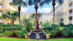 A courtyard with a central red lighthouse, surrounded by palm trees and various plants, with a building in the background. - 2BD/2BATH Villa! Near Beach! HHR Building 1! (Hilton Head Island)