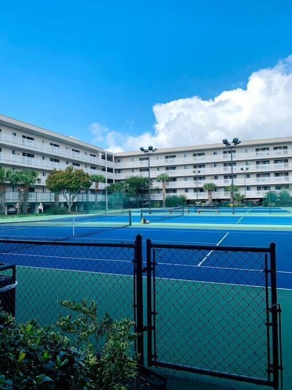 A multi-story building with a tennis court in front.