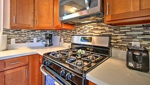 A kitchen with wooden cabinets, a stainless steel microwave, a gas stove, and a toaster. - Fort Gratiot Lake House on Lake Huron w/ Patio & Deck! (Fort Gratiot Township)