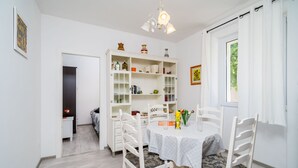 Ein Essbereich mit einem runden Tisch, weißen Stühlen, einem weißen Schrank mit Glastüren und einem Fenster mit Vorhängen.