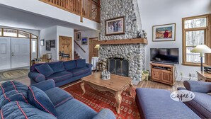 A spacious living room with a stone fireplace, wooden ceiling, and a large TV.