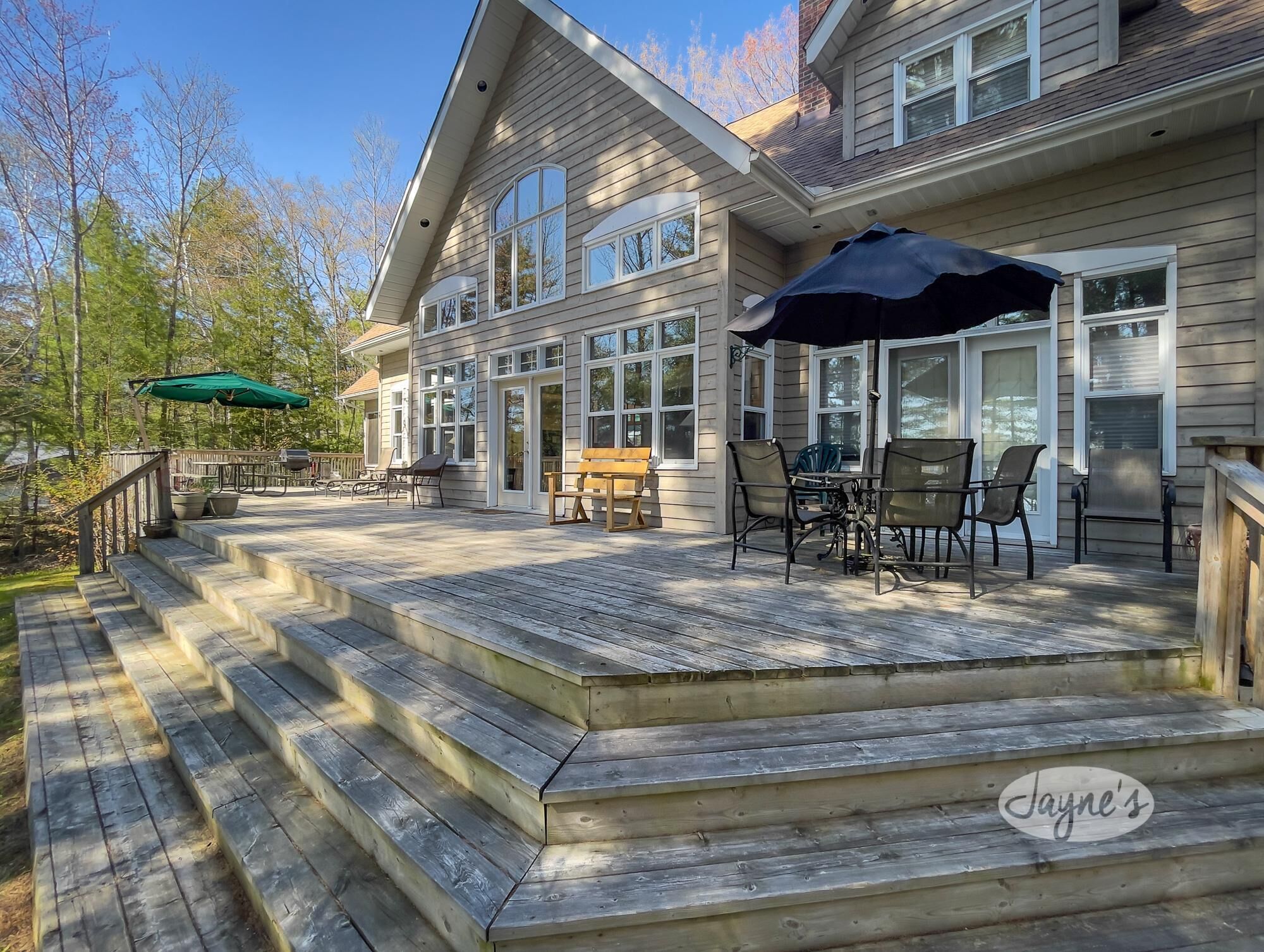 A wooden deck with outdoor furniture, a staircase, and a large house with multiple windows.