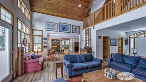 A spacious living room with high ceilings, wooden beams, and large windows.