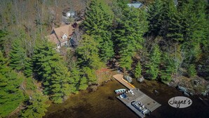 An aerial view of a cabin surrounded by dense forest, with a dock extending into a body of water.