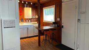 A compact kitchen with wooden cabinets, a central island with stools, a window, and a door. - Ocean Beach #3, Breeze, Retro/Cozy, Studio Cottage only 3 blocks to beach!⛱ (San Diego)