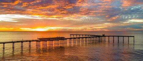 A pier extending into calm waters with a sunset in the background.