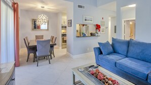 A modern living room with a blue sofa, a dining area with a chandelier, and a kitchen in the background. - Few days still available this winter! King-size bed. Free parking. Renovated! (Clearwater)