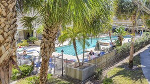 A pool area with lounge chairs and umbrellas, surrounded by palm trees and a fence. - Few days still available this winter! King-size bed. Free parking. Renovated! (Clearwater)