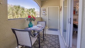A dining area with a table set for two, a vase with flowers, and a view of palm trees through a window. - Few days still available this winter! King-size bed. Free parking. Renovated! (Clearwater)