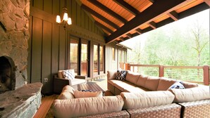 A cozy outdoor seating area with a stone fireplace, cushioned sofas, and a wooden deck. - River's Edge Retreat by North Bend Escapes (Fall City)