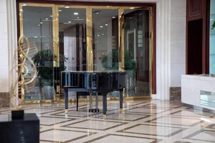 Un piano de cola en un vestíbulo con piso de baldosas geométricas y entrada por puerta de vidrio.