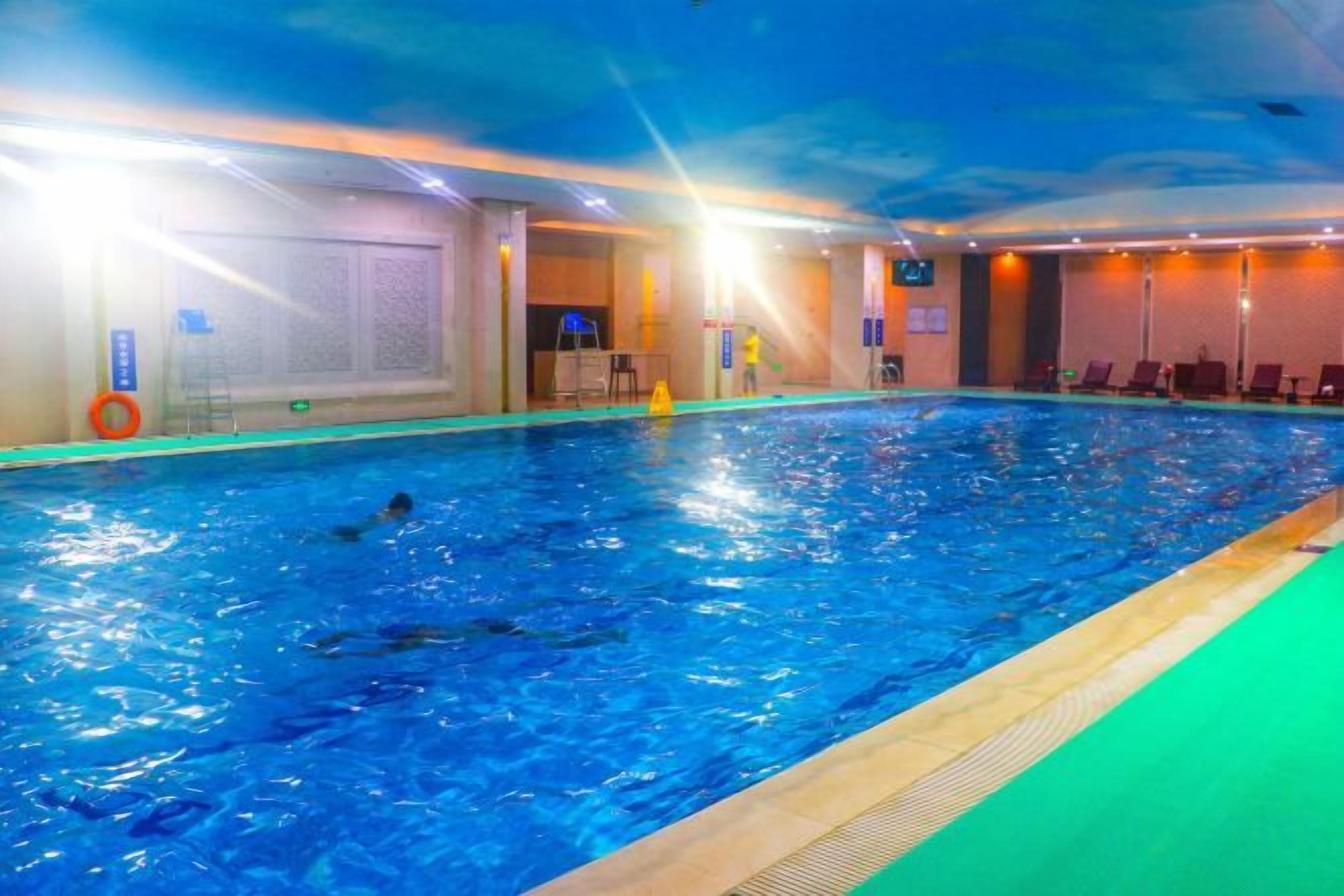 An indoor swimming pool with clear water, a diving board, and lounge chairs along the poolside.
