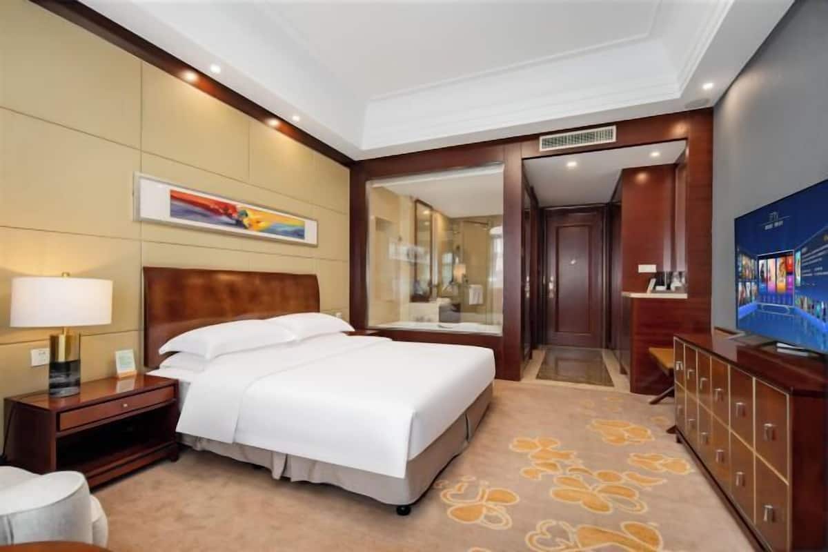 A hotel room with a bed, a nightstand, a TV, a dresser, and a mirror.